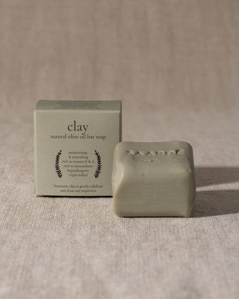 Clay natural olive oil bar soap with packaging on a beige fabric background