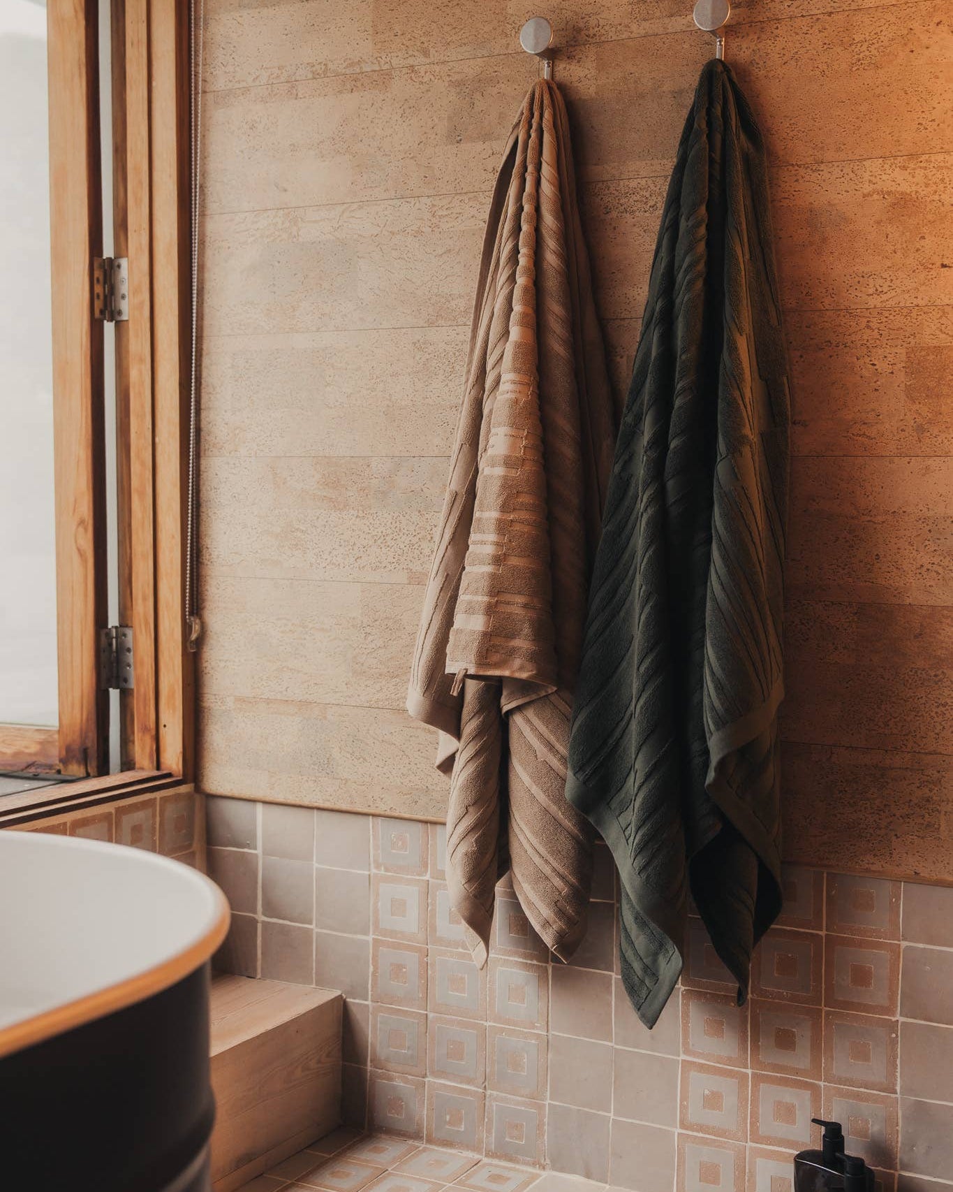 Towels hanging on hooks against a tiled bathroom wall.