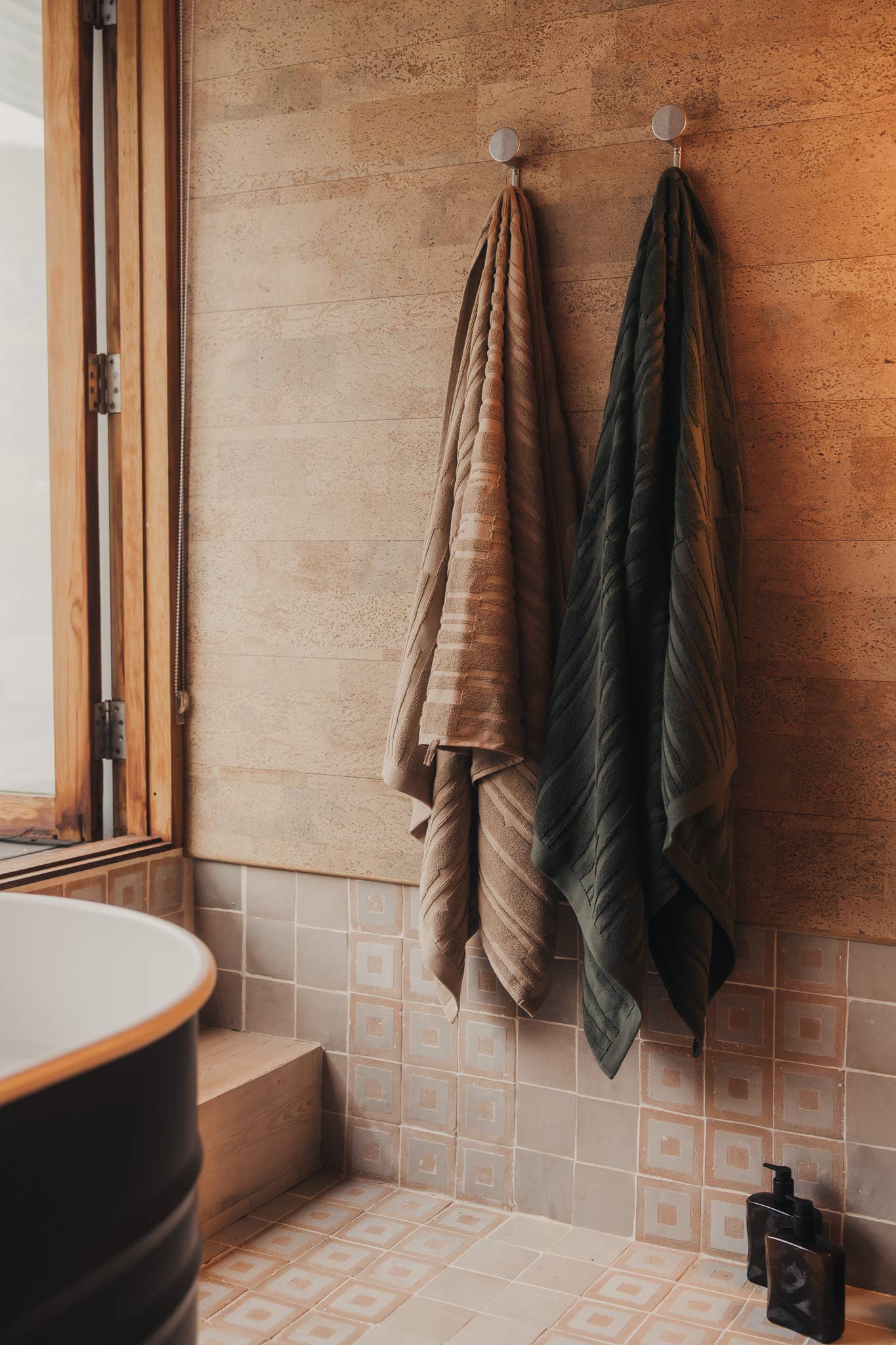 Towels hanging on hooks against a tiled bathroom wall.