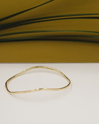wavy hand forged brass bracelet styled with gold background and grass