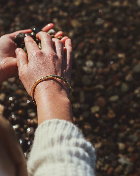 Hands holding pebbles model wearing brass bracelet