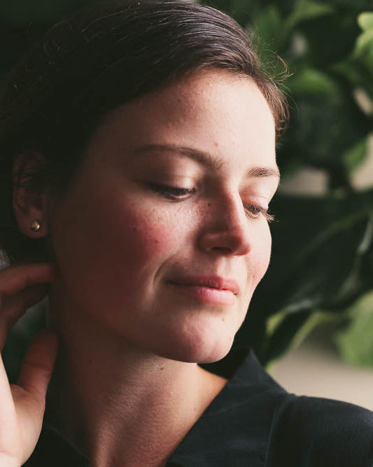model wearing gold stud earrings that are cast from a pebble