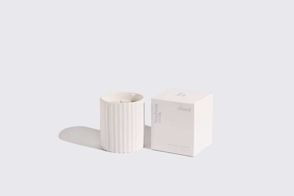 White candle with ribbed texture next to its packaging on a light gray background