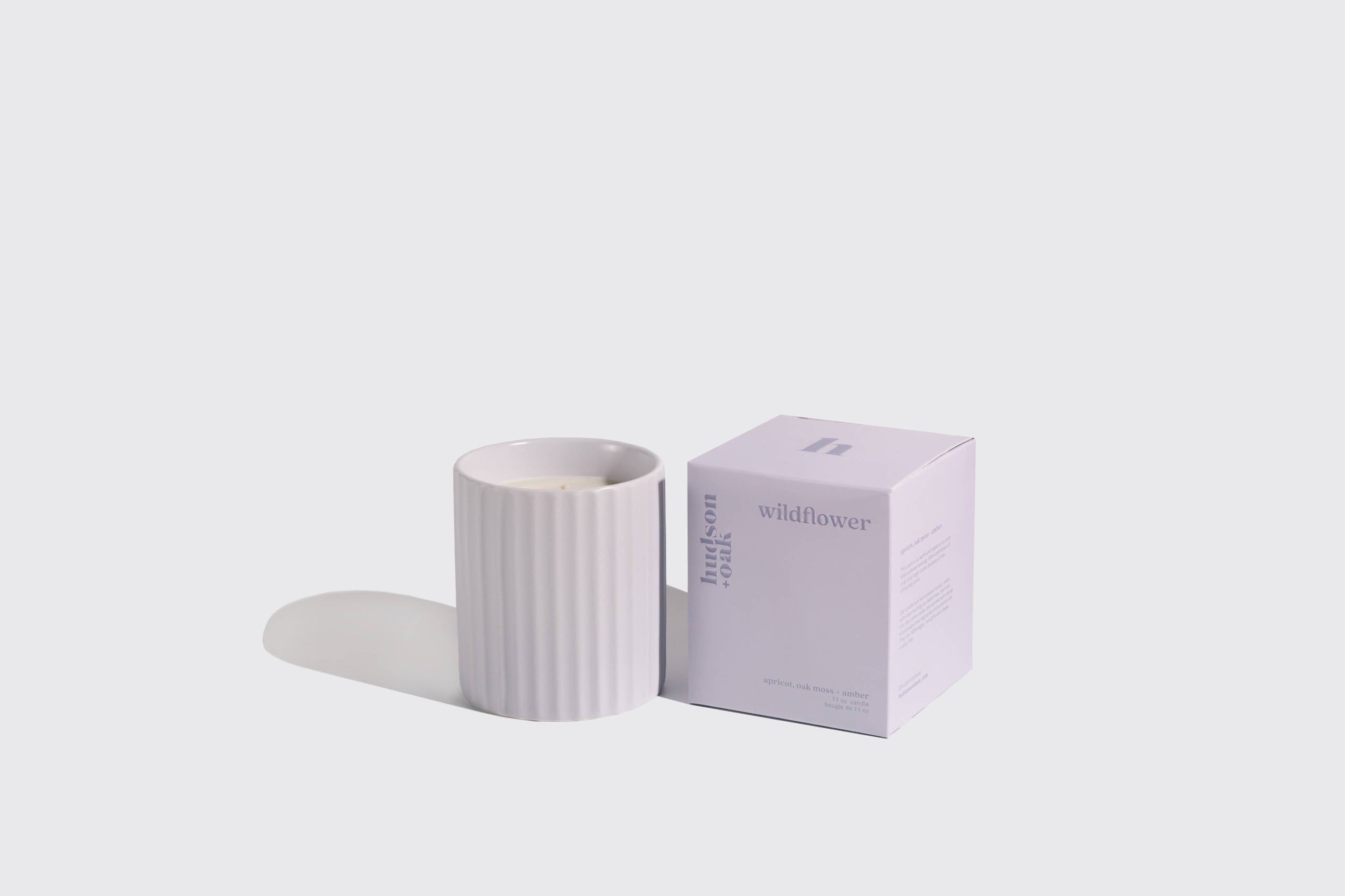 White candle with striped pattern and matching box on a light gray background