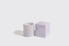 White candle with striped pattern and matching box on a light gray background