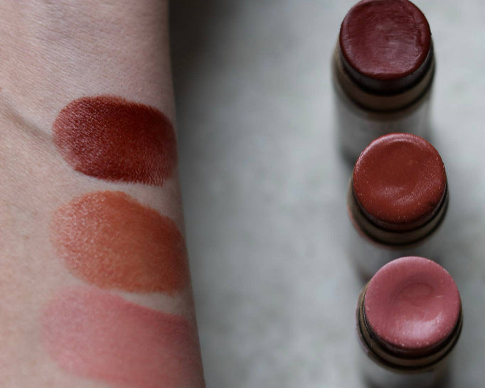 Lipstick swatches on a person's arm next to lipstick tubes on a marble surface