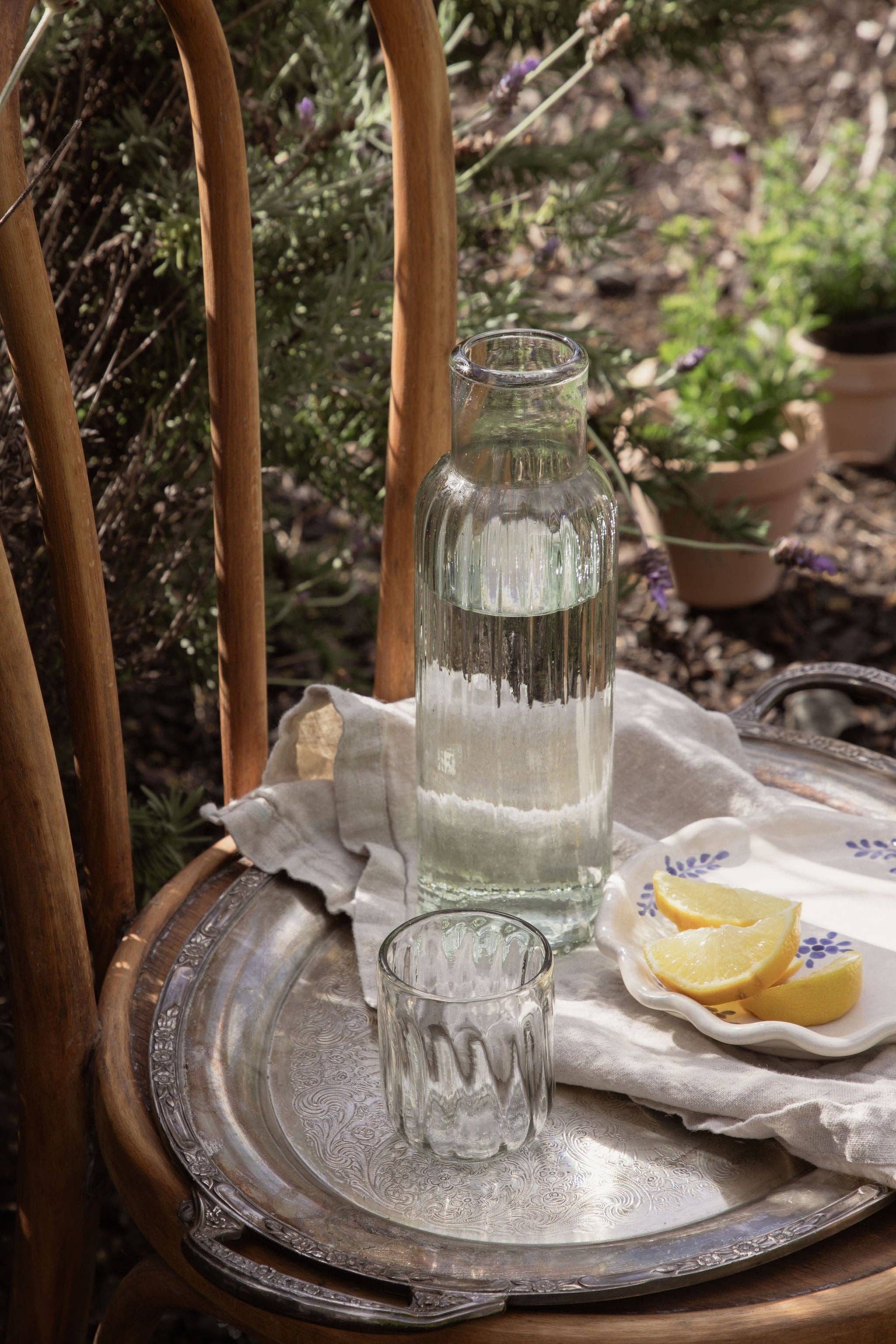 Tray with a glass, lemon slices, and a vase on a natural outdoor setting
