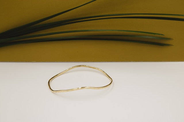 wavy hand forged brass bracelet styled with gold background and grass